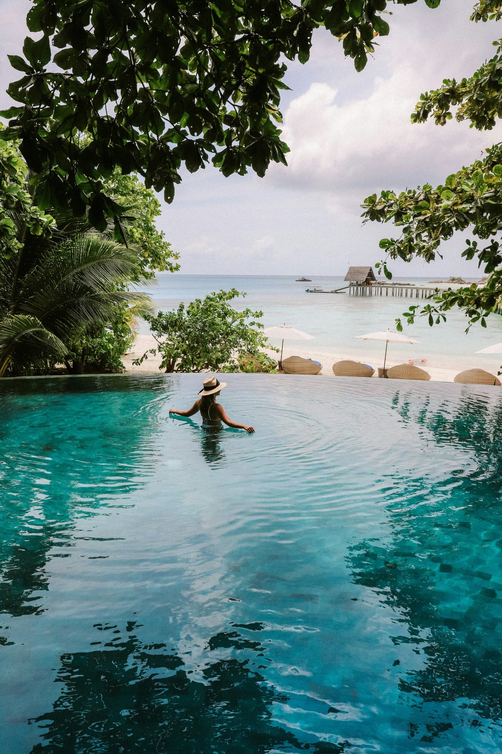 The Maldives with a person in an infinity pool overlooking the ocean. It is one of the Luxury beach vacations you can book with me.